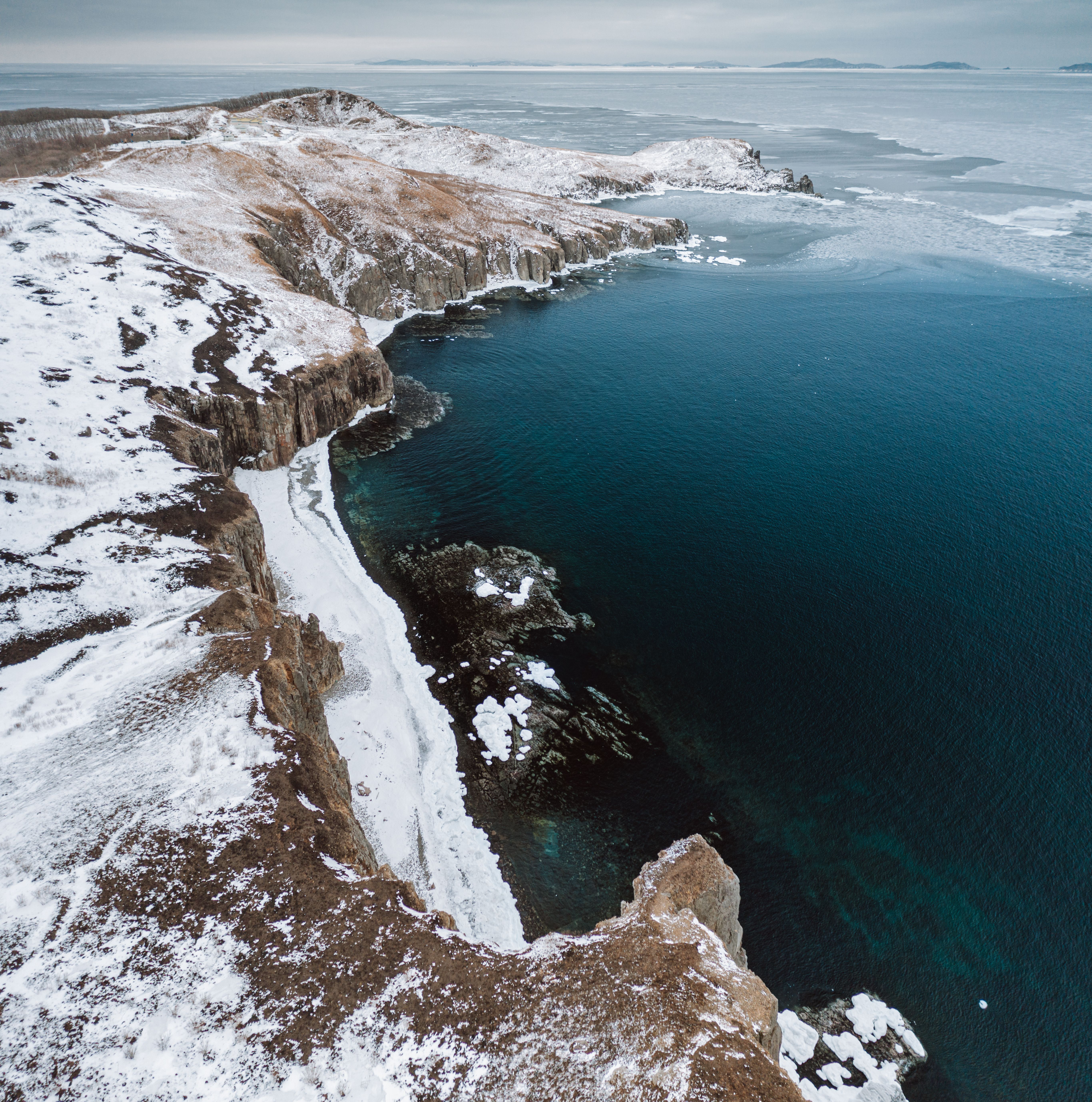 A breathtaking aerial view of the snowy coastline and deep blue sea in Khasansky District, Russia.