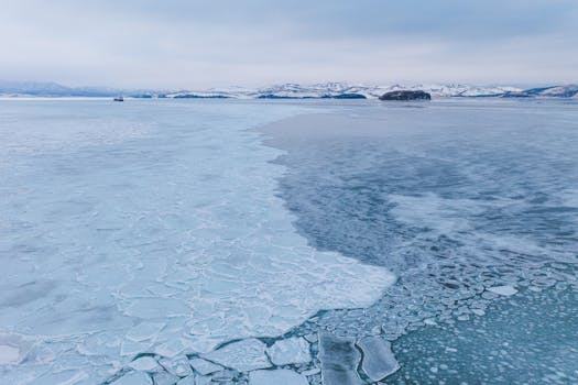 A stunning aerial view capturing the vastness of the frozen Arctic landscape with icy waters and distant snow-covered hills.