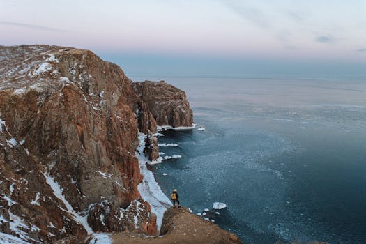 Explore the dramatic snow-dusted cliffs of Russkiy Island with a lone adventurer gazing into the icy sea.