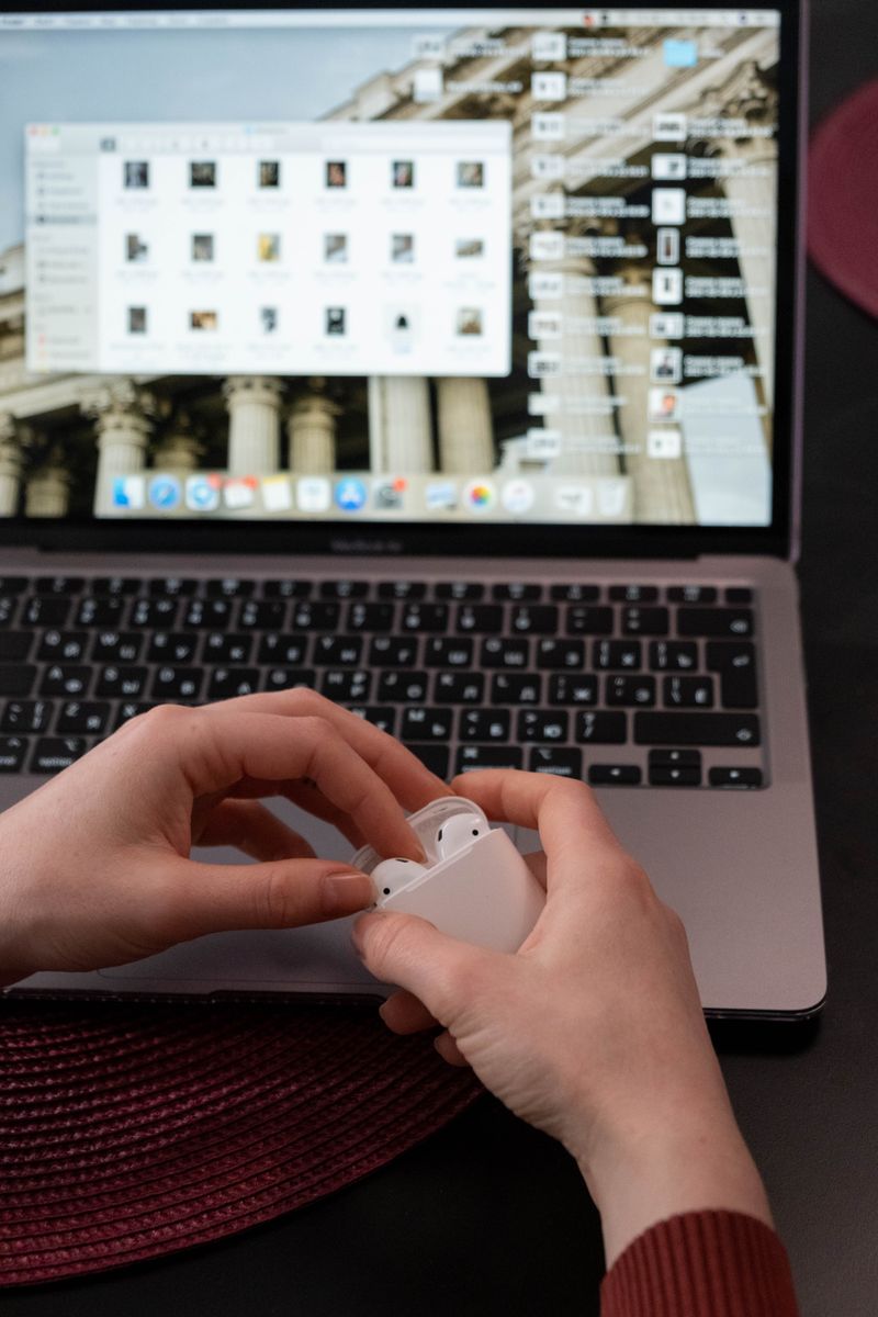 Hands holding wireless earbuds near an open laptop screen