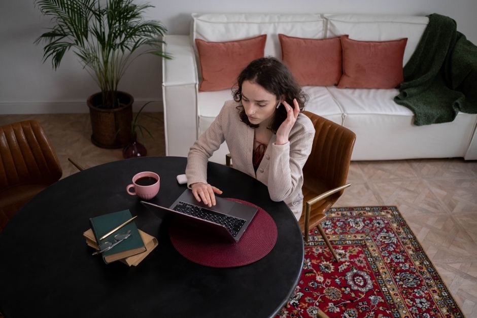 Woman working on a laptop at home with coffee and headphones, creating a cozy work atmosphere.