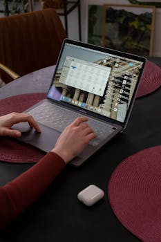 Close-up of hands typing on a laptop with apps open, showcasing a cozy workspace.