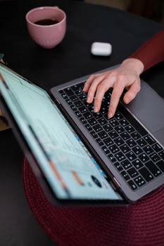 Close-up of hands typing on a laptop with a pink cup and earphones nearby, indoor setting.