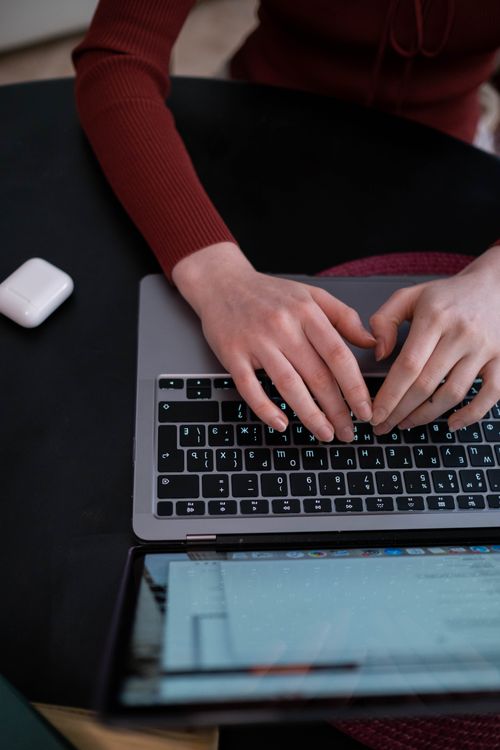 Free Person typing on a laptop keyboard indoors with AirPods nearby Stock Photo