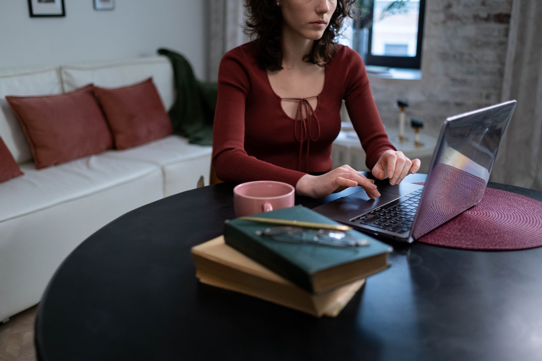 A woman is typing on a laptop at a round black table in a stylish, comfortable room.