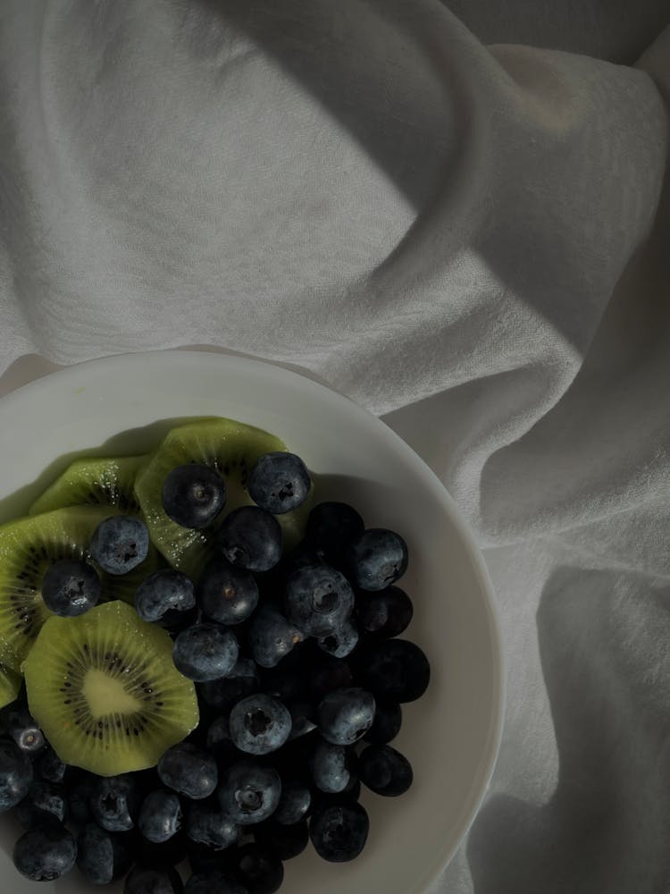 Blueberries And Kiwi In Plate On White Fabric