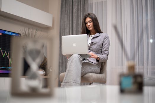 Woman working indoors on a laptop analyzing stock charts, in a modern setting.