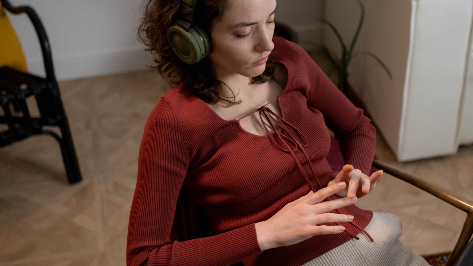 A woman seated indoors with her eyes closed while listening through over-ear headphones