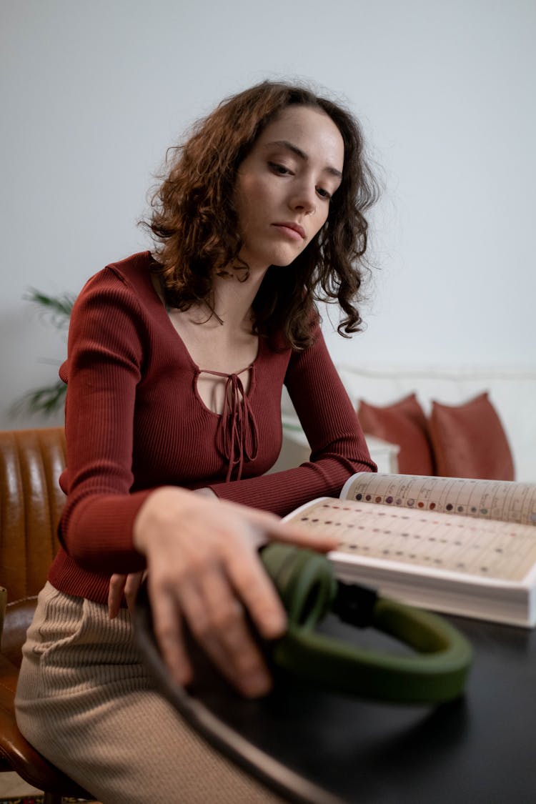 Woman Sitting By Table With Book And Headphones