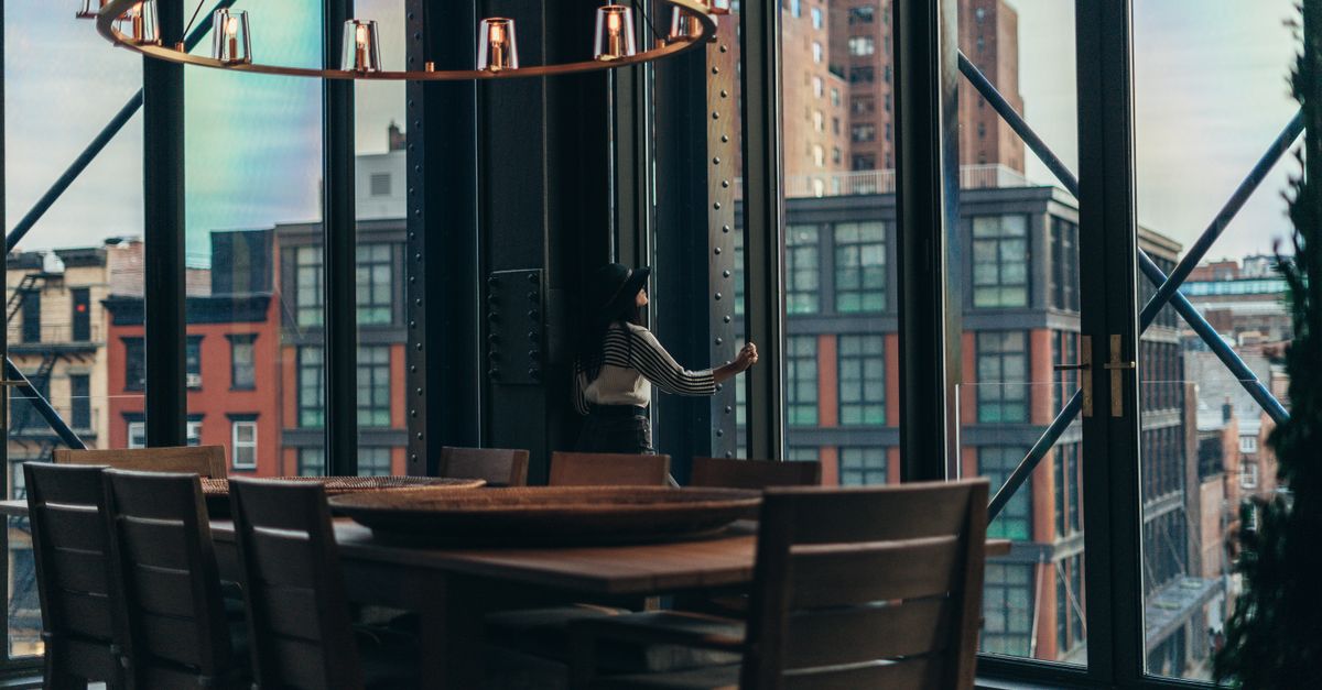 a person standing confidently with good posture looking out a large window at a city skyline