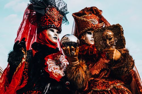 Free Two elaborately dressed participants at the Venetian Carnival in stunning red costumes and masks. Stock Photo