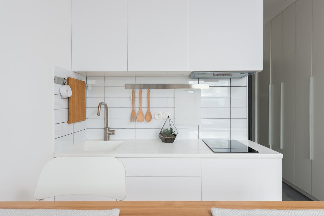 Free Wooden table placed near white cupboards in modern kitchen with minimalist interior in daylight Stock Photo