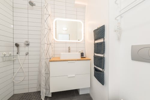 Interior of contemporary bathroom with white furniture and shower cabin near illuminated mirror and ceramic sink