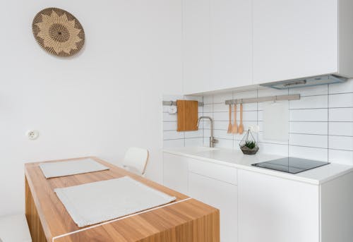 Wooden table with chairs in contemporary kitchen with white cabinets and modern appliances in daylight