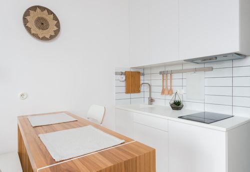 Free Wooden table with chairs in contemporary kitchen with white cabinets and modern appliances in daylight Stock Photo