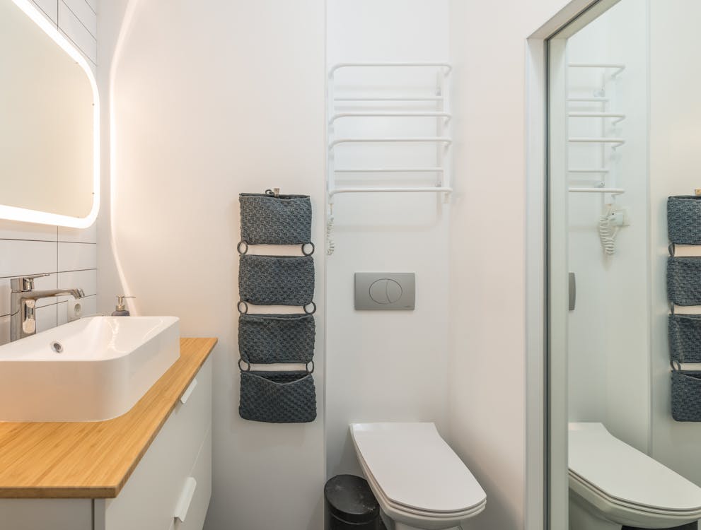 Small modern bathroom with ceramic toilet bowl and sink under illuminated mirror in modern apartment