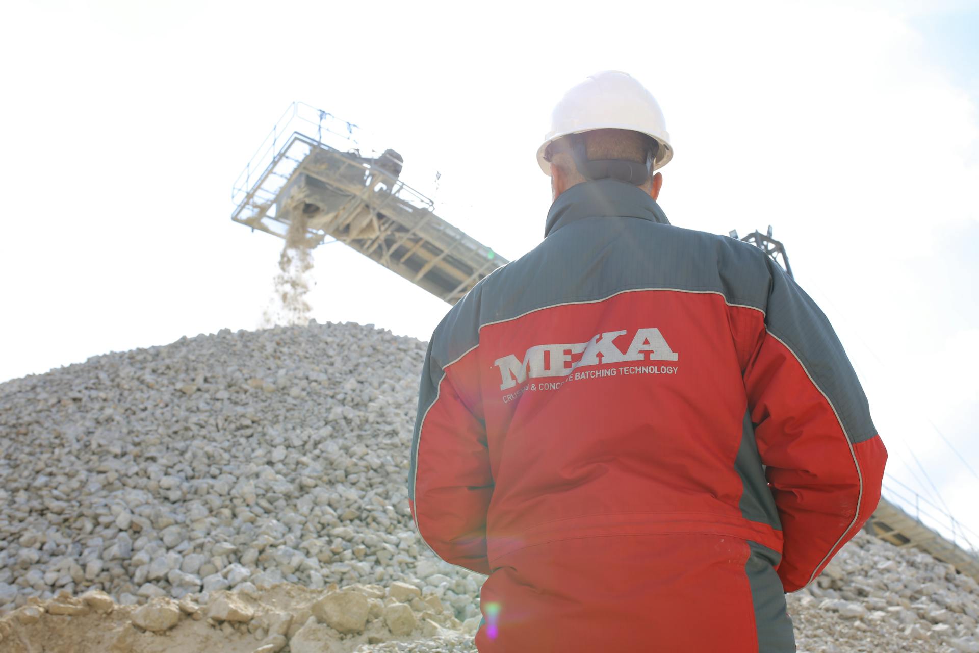 Back view of a construction worker in Ankara quarry observing a conveyor belt at a gravel site.