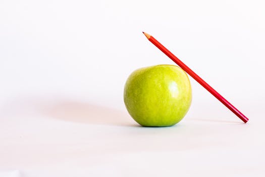 Close-up of a green apple with a red colored pencil against a white background.
