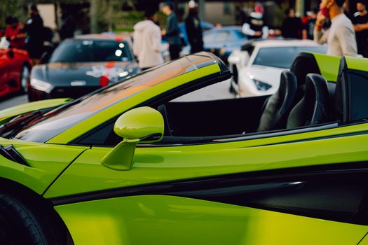 A striking green convertible sports car parked at an outdoor car show with blurred background.