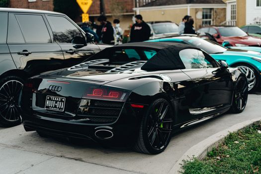 Black Audi R8 parked at a lively car show, surrounded by spectators and luxury cars.
