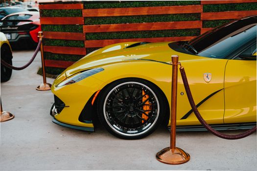Front side view of a vibrant yellow Ferrari showcased at an exclusive outdoor car event.