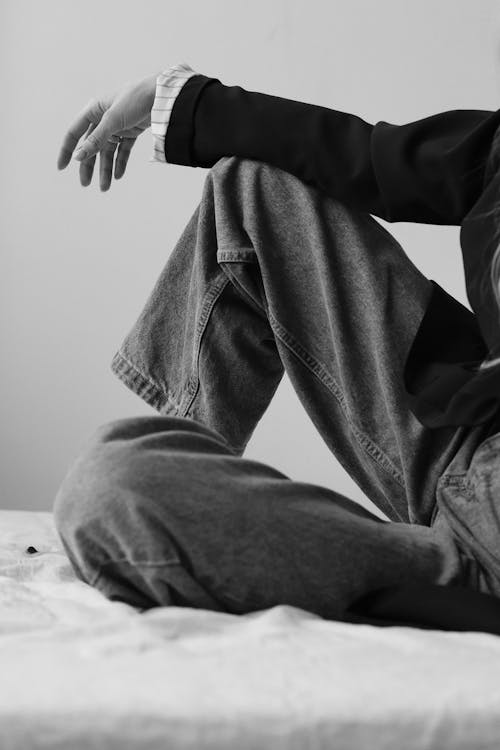 Person in Black Jacket and Denim Jeans Sitting on Bed