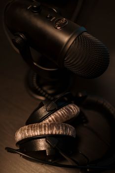 Close-up of a black microphone and headphones on a dark surface, ideal for podcasting or studio work.