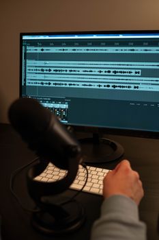 Close-up of a hand working in an audio recording studio with microphone and monitor.