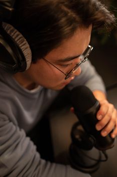 Asian man recording podcast using microphone and headphones indoors
