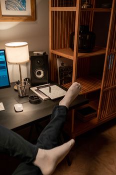 Cozy home office setup featuring feet on desk, speaker, and warm lighting.