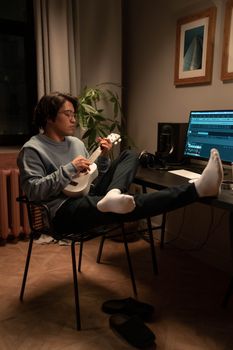 Asian man enjoying ukulele music at home sound studio, blending relaxation and creativity.