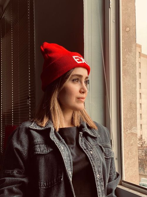 Free A fashionable woman wearing a red beanie gazes thoughtfully out the window, capturing a modern and stylish look. Stock Photo