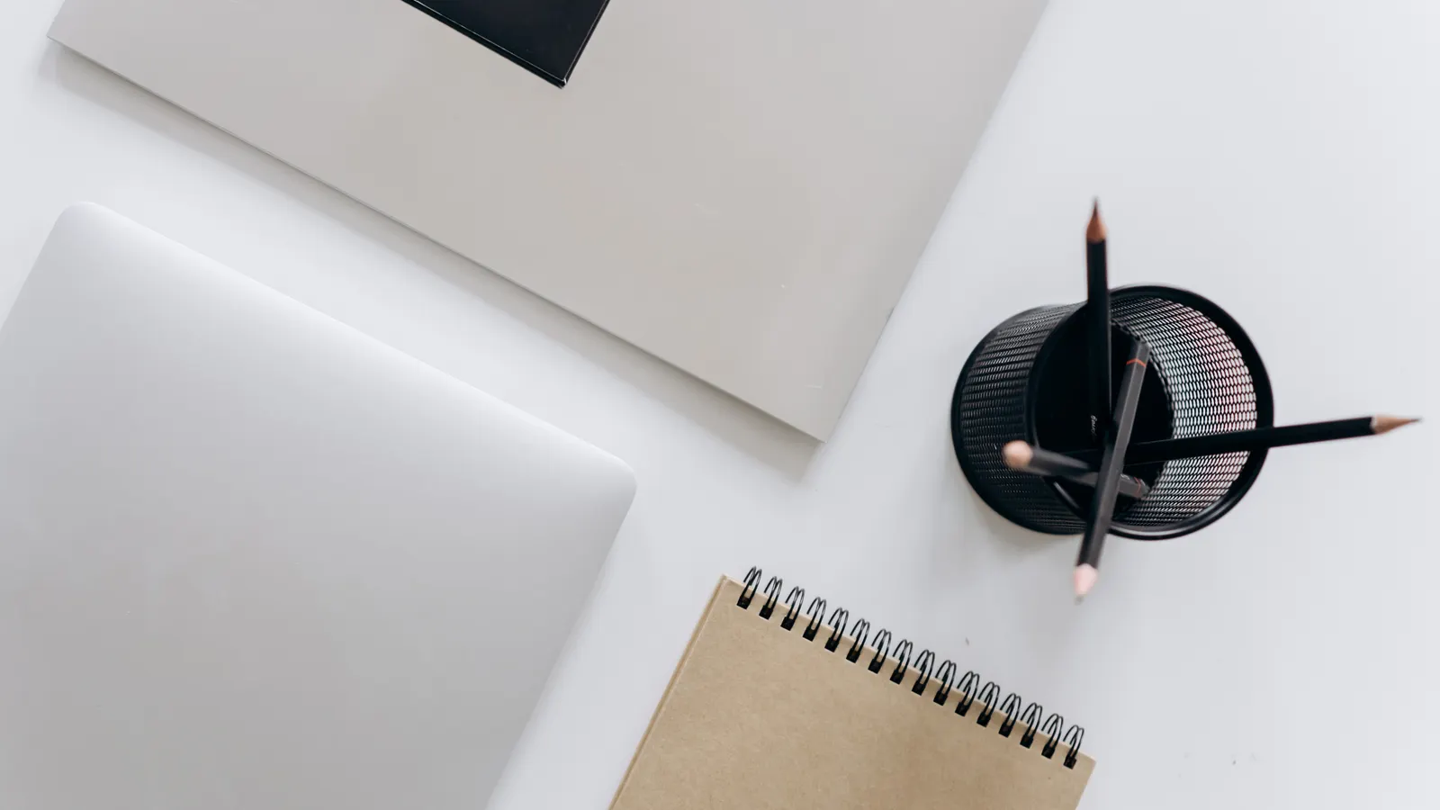 A minimalist workspace with a laptop, notepad, and a small set of stationery arranged on a desk