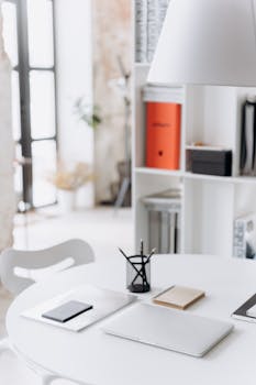 Clean and modern workspace featuring a laptop, notepad, and pen in a bright, minimalist setting.