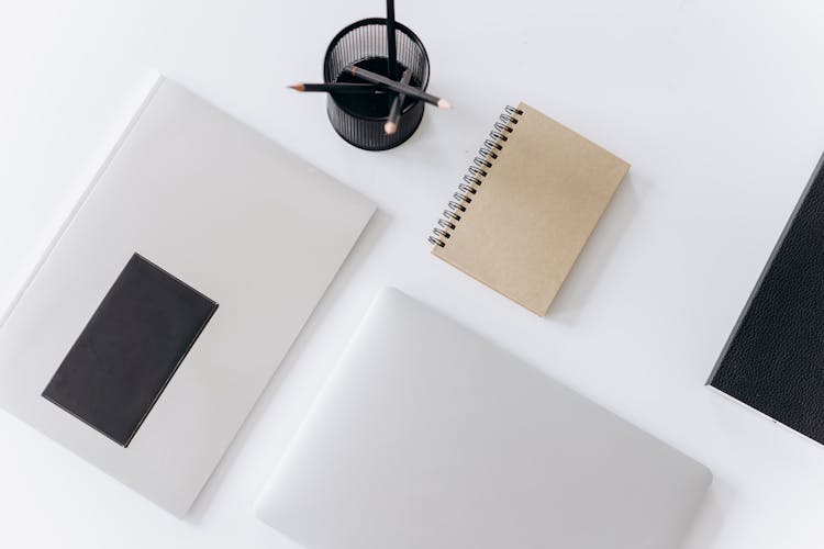 Netbook With Planner And Jotter Placed Near Pencils On Desk