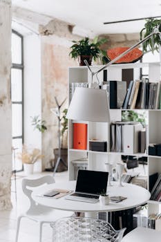 Stylish office corner with laptop, books, and greenery in a minimalist design.