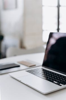 Minimalistic workspace featuring a laptop and smartphone on a white table in an office setting.