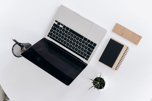 Modern minimalist workspace featuring a laptop, notebook, and plant on a white surface.