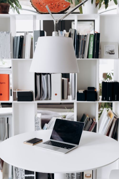 Free A modern minimalist workspace featuring a laptop, smartphone, and organized bookshelf under ambient lighting. Stock Photo