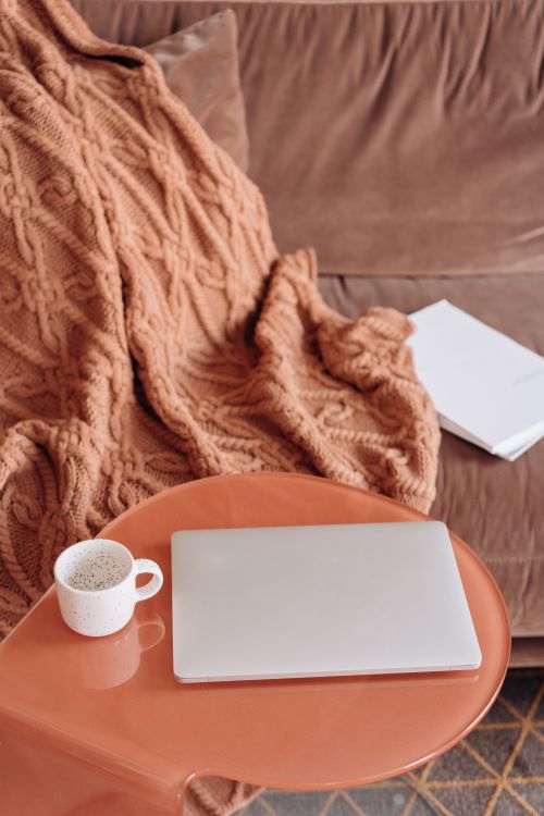 Free A warm and cozy home setting with a laptop and coffee on a wooden table next to a knitted blanket. Stock Photo