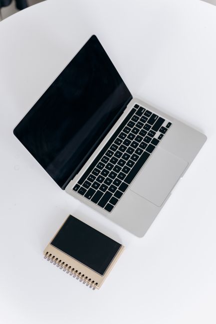 Fotomural Vista cenital de un portátil elegante y un cuaderno sobre una mesa blanca, ideal para un espacio de trabajo minimalista.