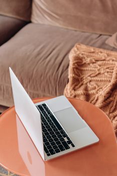 A modern laptop on a coral table next to a knitted throw, creating a warm, cozy home office vibe.