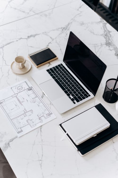 Free Overhead view of a modern desk with laptop, blueprint, and stationery on a marble surface. Stock Photo