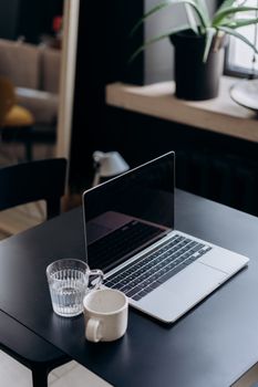 A minimalist workspace featuring a laptop, glass of water, and plant on a dark table.