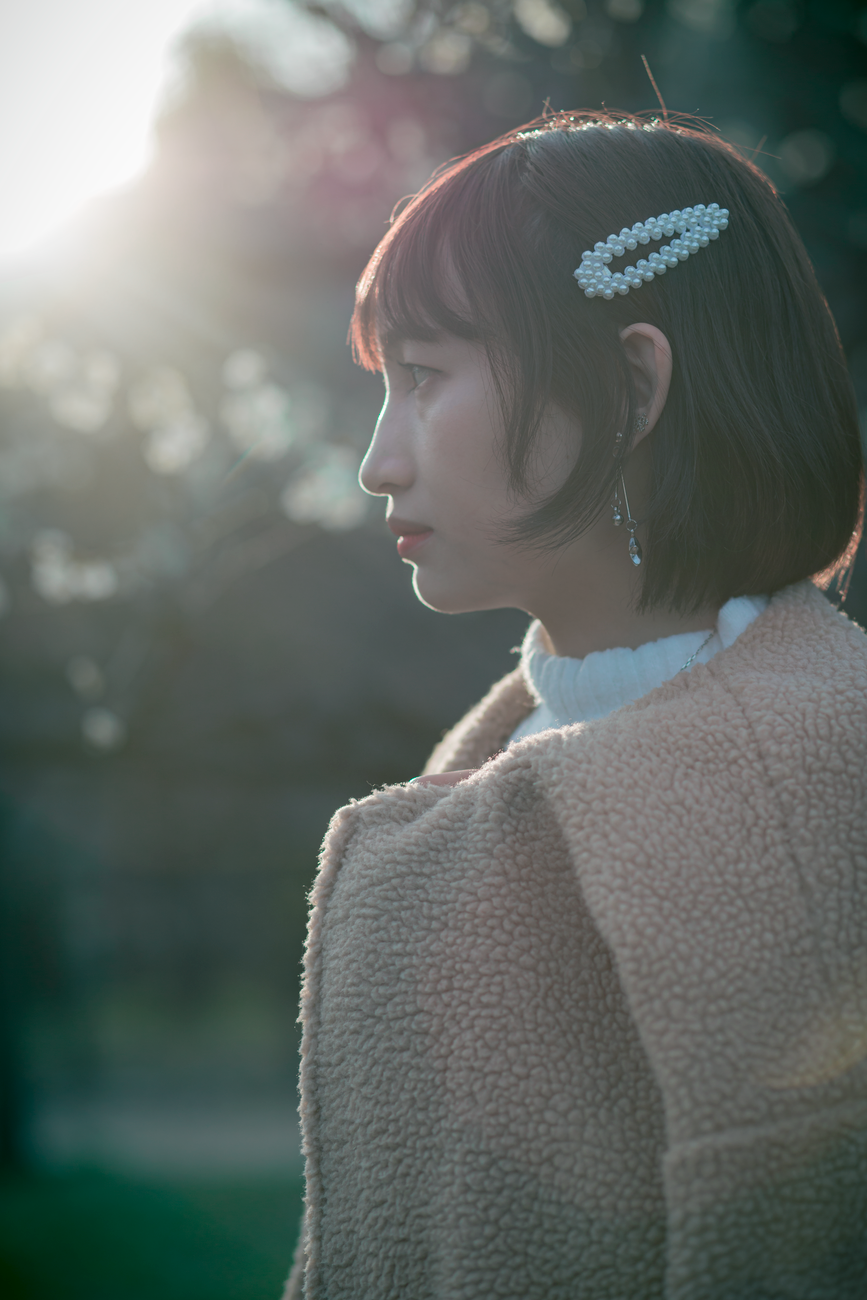 A side profile of a woman in a wool coat with sunlight highlighting her features outdoors.