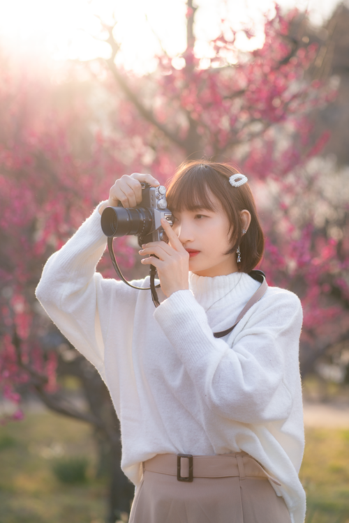 Free Stylish Asian woman capturing nature with a camera in a vibrant blossom garden during spring. Stock Photo