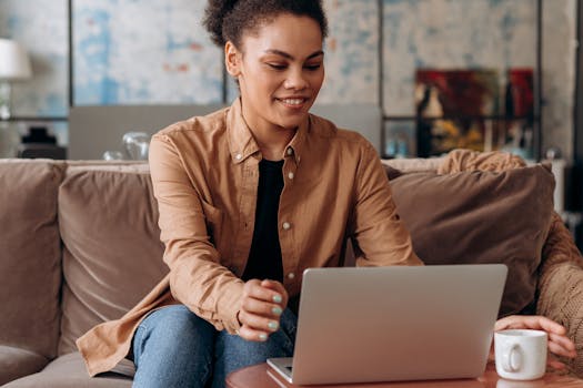 Smiling African American woman working from home on a laptop, sitting comfortably in a cozy living room.