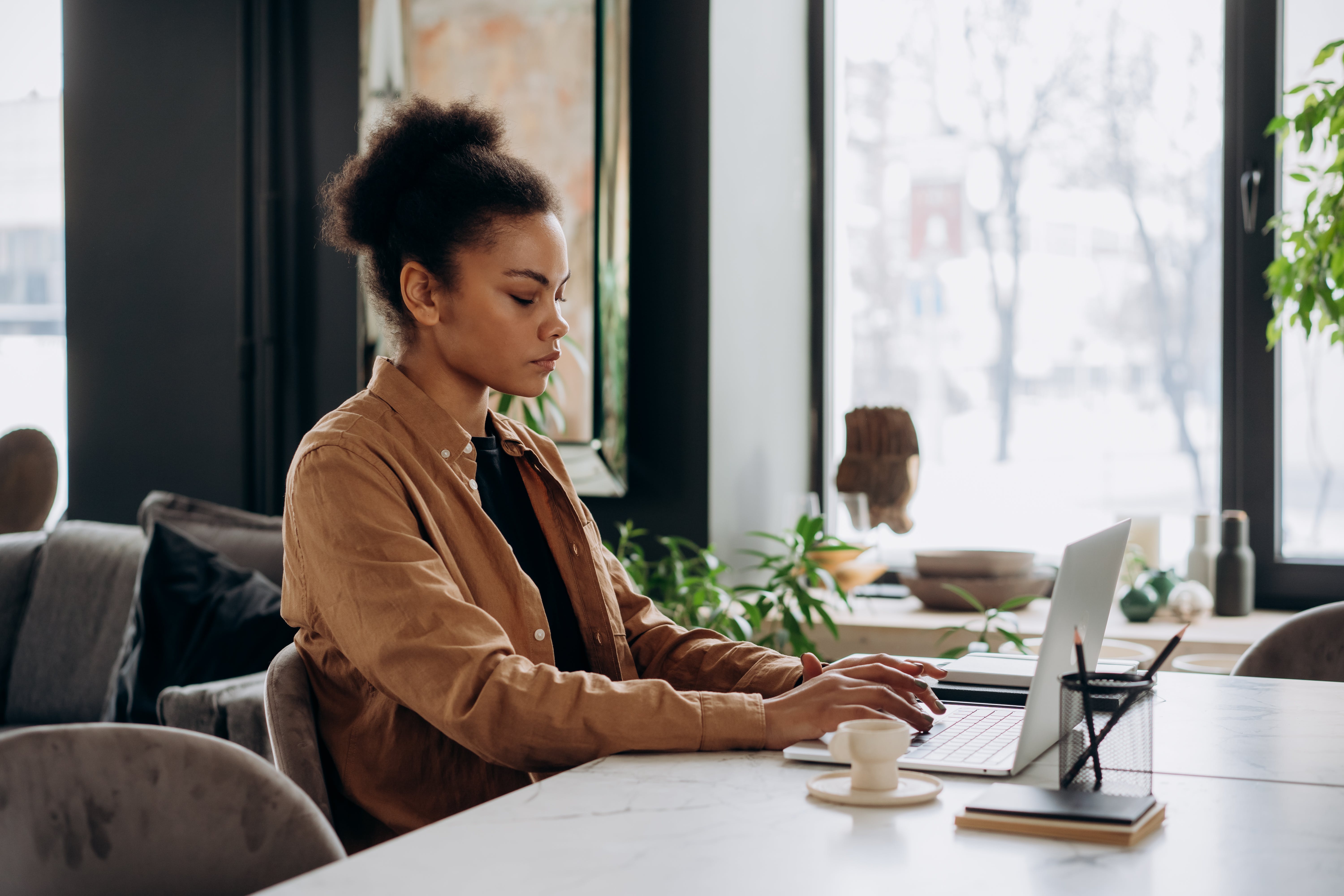 woman in a brown long sleeve shirt typing on her laptop