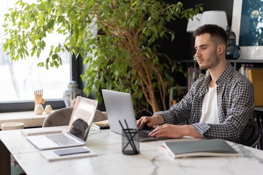Young man working on a laptop in a stylish indoor office setting with greenery.