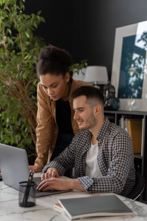Free Two colleagues work together on a laptop in a modern office setting. Stock Photo